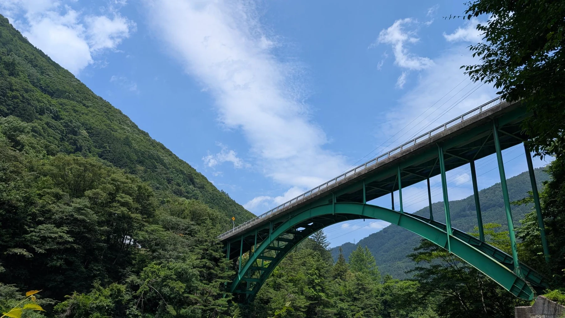 緑の山々の間に架かる鋼製アーチ橋