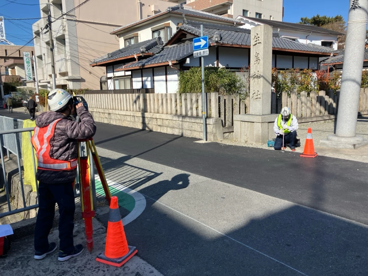 道路沿いで測量機器と標尺を使い調査を行う二人の技術者